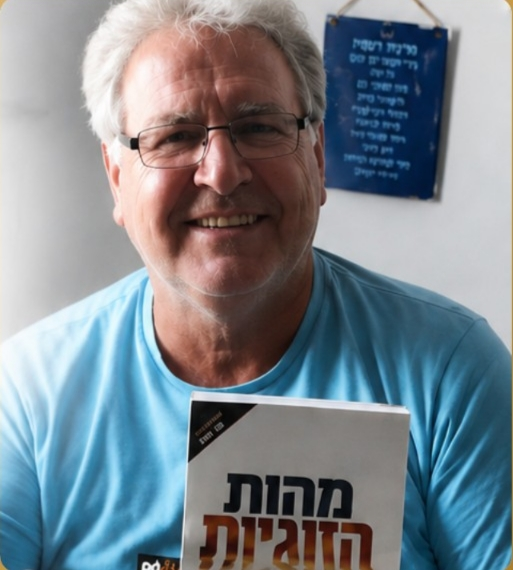 איציק ברבי מחייך בחולצה כחולה ומחזיק את הספר מהות הזוגיות